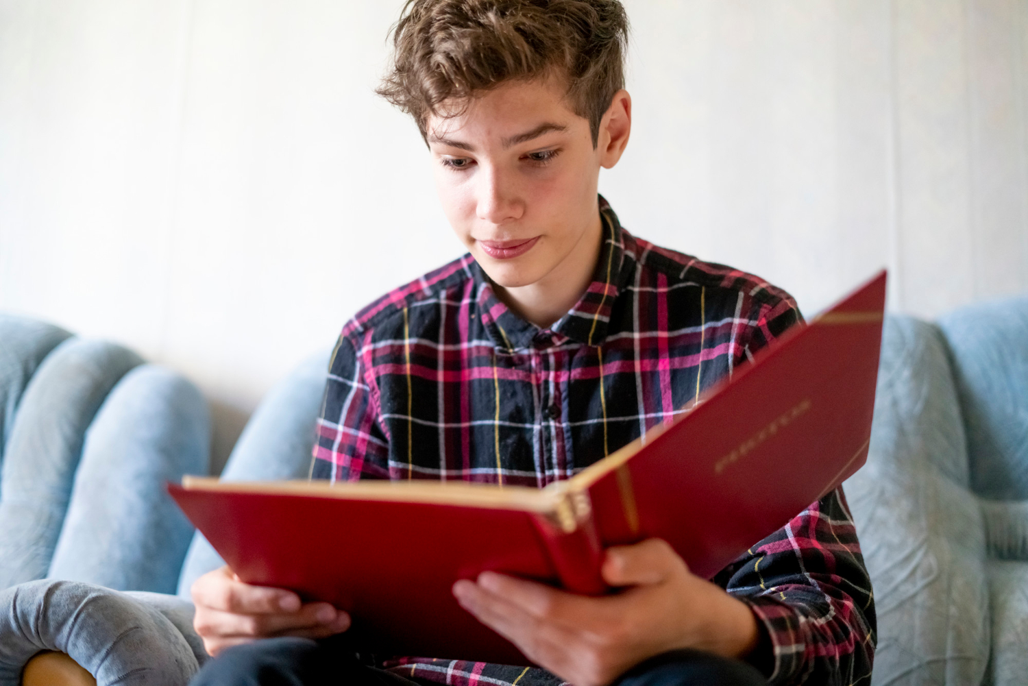 un adolescent est en train de lire un livre sur un canapé
